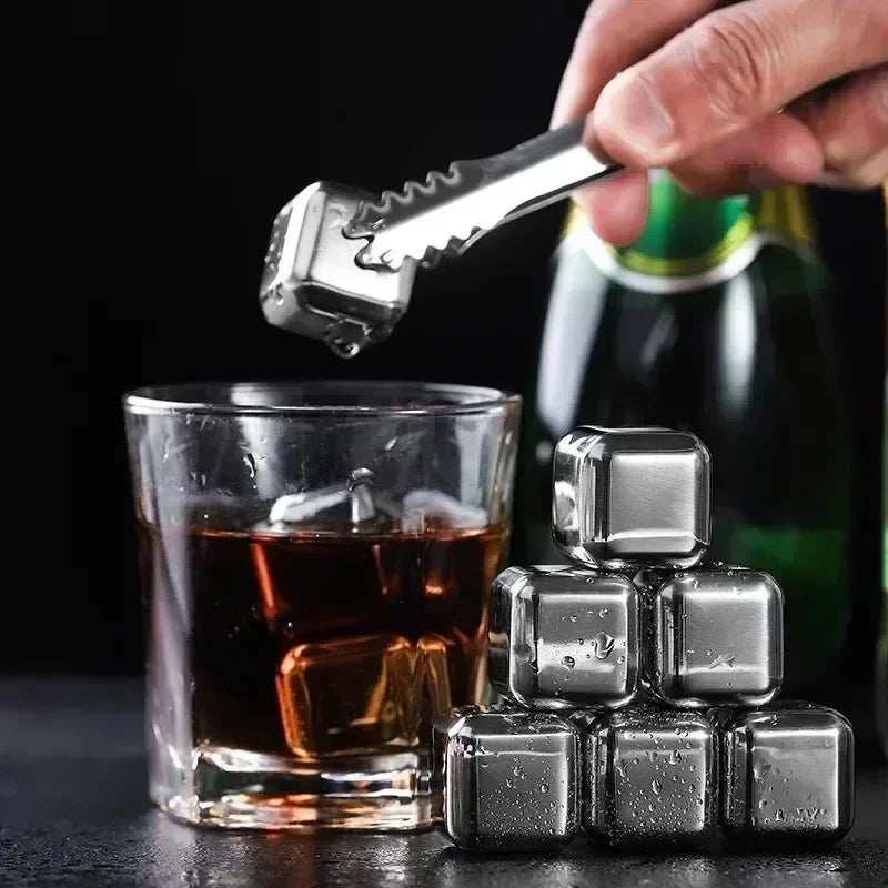 A hand holds a silver key above a glass of whiskey and several reusable stainless steel ice cubes.