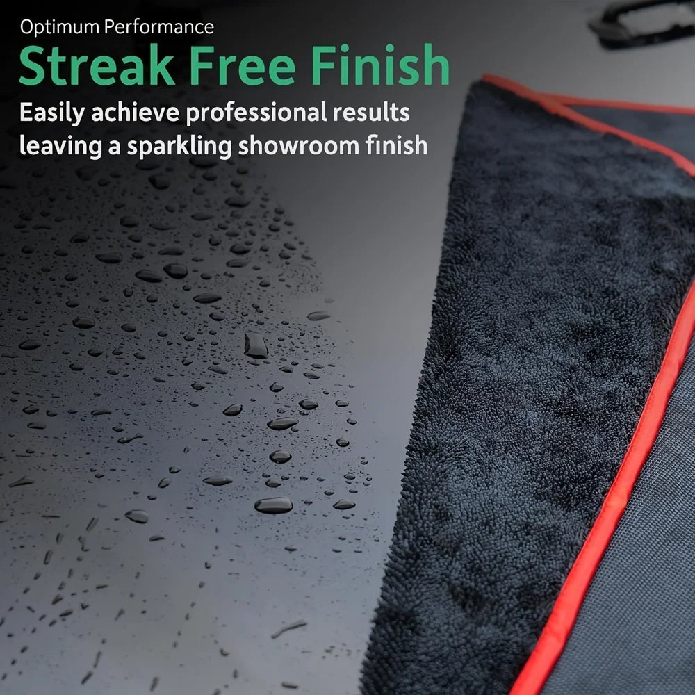 A black microfiber car drying towel with an orange trim is shown next to a wet, glossy surface.