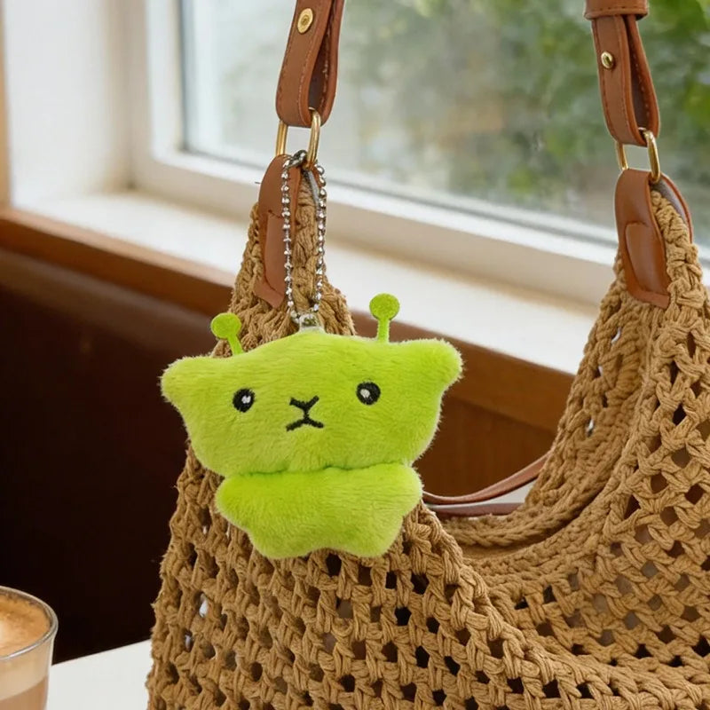 A light green plush cat keychain is displayed hanging from a brown woven bag.