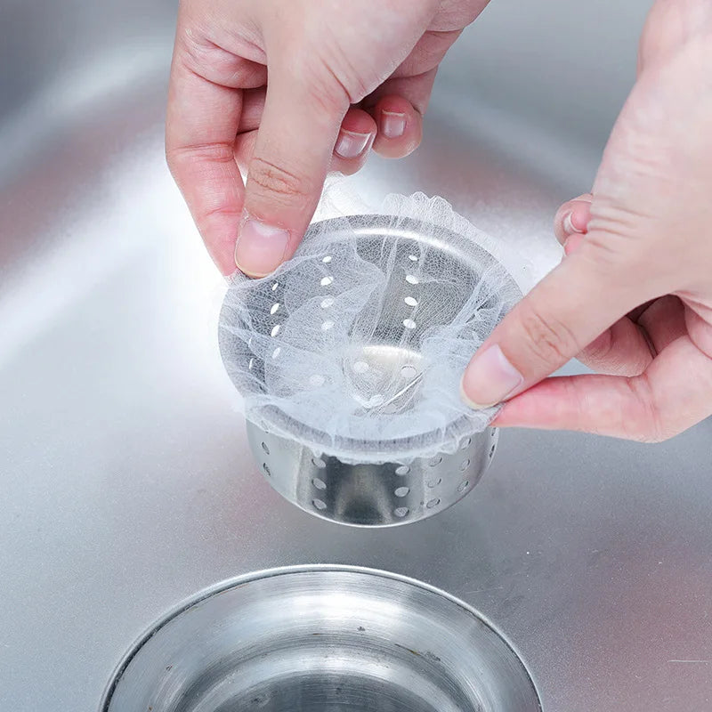 A hand is placing a disposable sink drain filter bag into a metal strainer or drain.