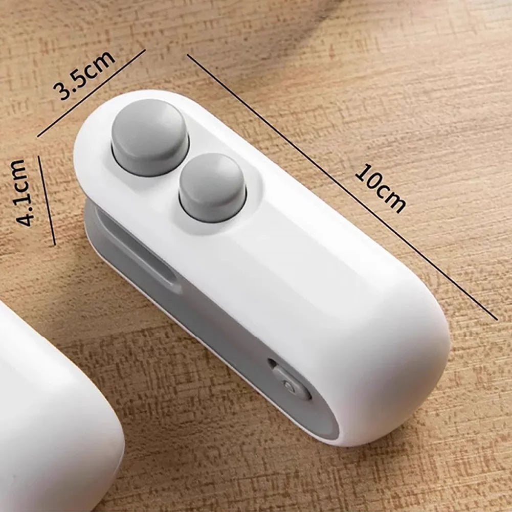 A white handheld bag sealer and cutter device with two round buttons shown on a wooden surface.
