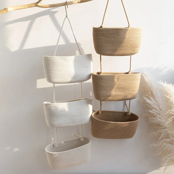 Handwoven multi-layer wall storage baskets in natural beige and off-white tones hanging against a white wall.