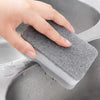 A hand is holding a gray, textured cleaning sponge inside a gray kitchen sink.