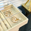 A light beige jewelry organizer box displaying gold and pearl rings and bracelets.