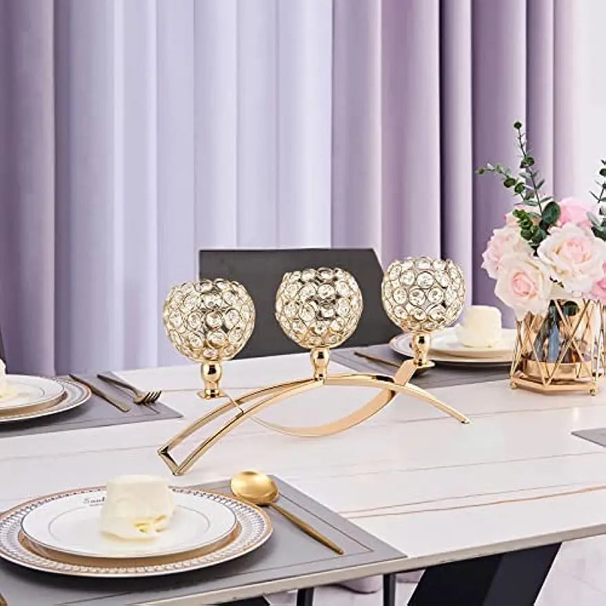 A gold crystal tealight candelabra set displayed on a white table with purple curtains.