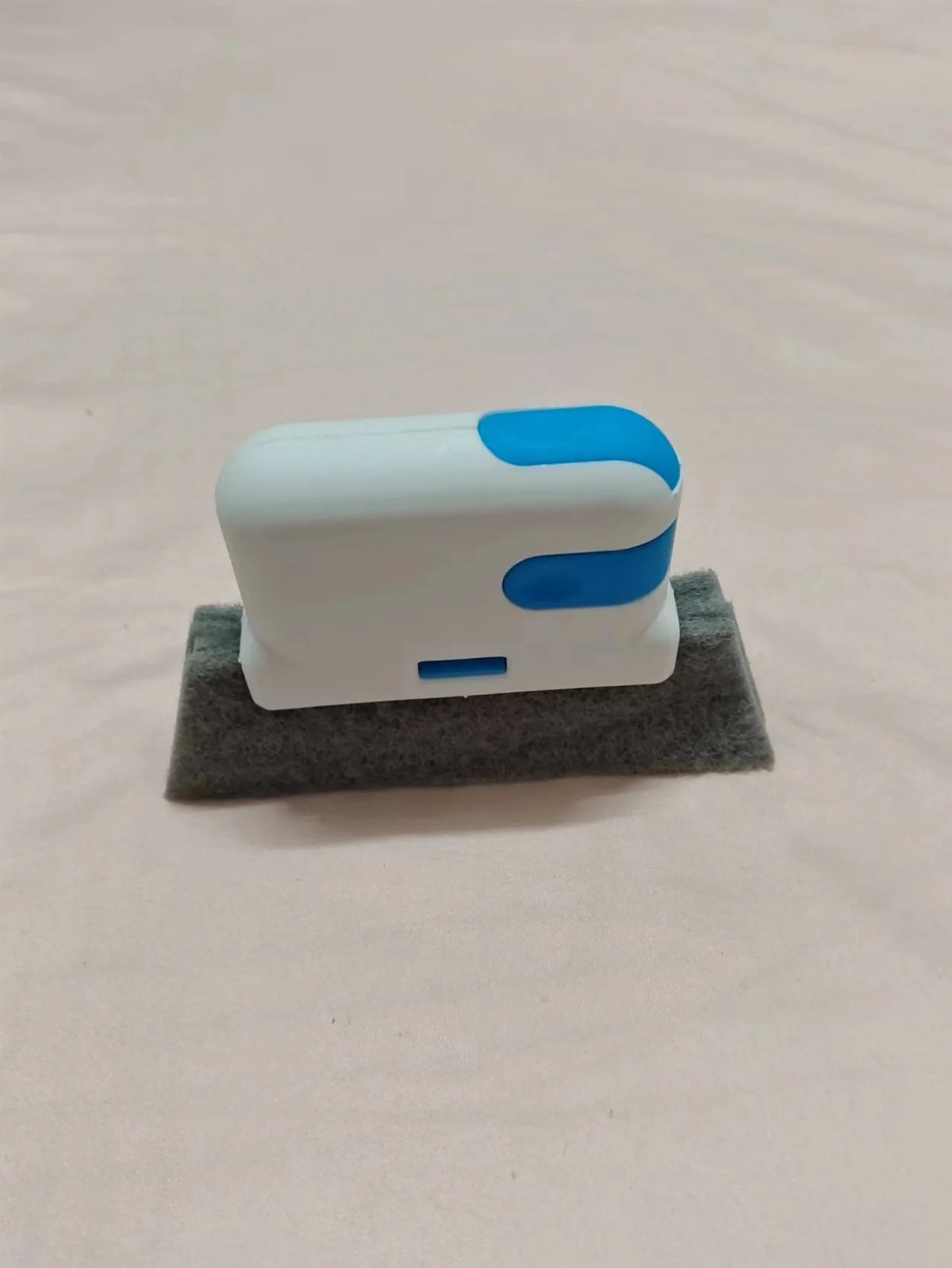Un cepillo de limpieza blanco con detalles azules descansa sobre una superficie de fieltro gris.