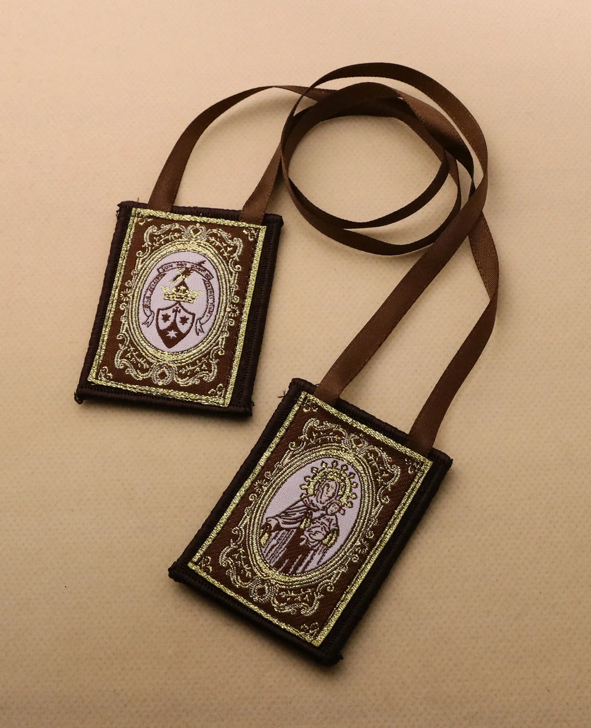 A brown leather scapular necklace with an embroidered design featuring a religious figure.