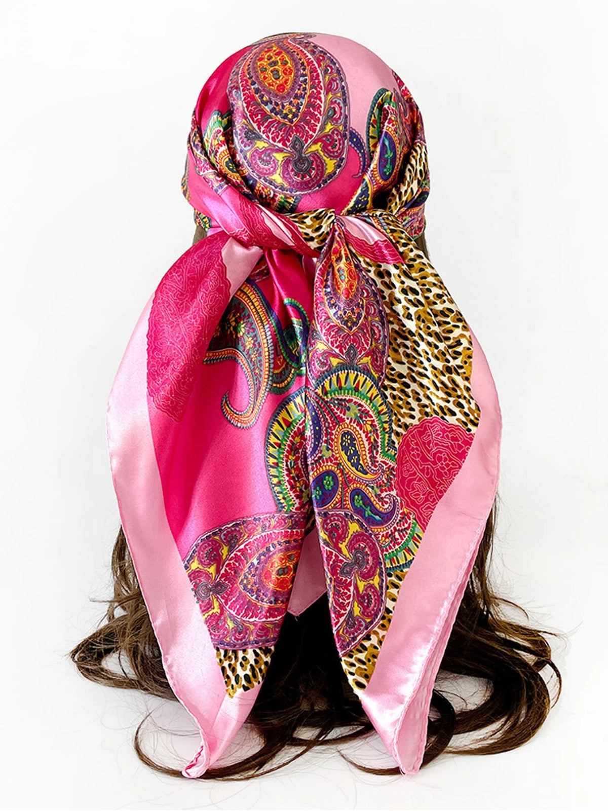 A vibrant pink scarf featuring a paisley print with leopard spots tied around a woman's hair.