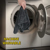 A hand is placing a dark gray microfiber drying towel into the drum of a white washing machine.