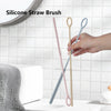 A hand is holding two silicone straw cleaning brushes, one pink and one light blue, against a white tiled background.