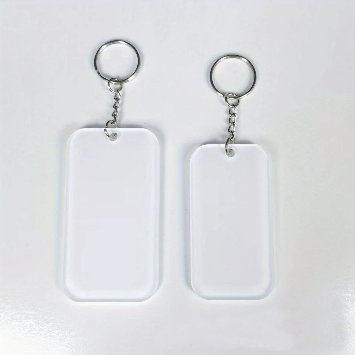 Two clear acrylic keychains with silver split rings and blank white rectangular tags.