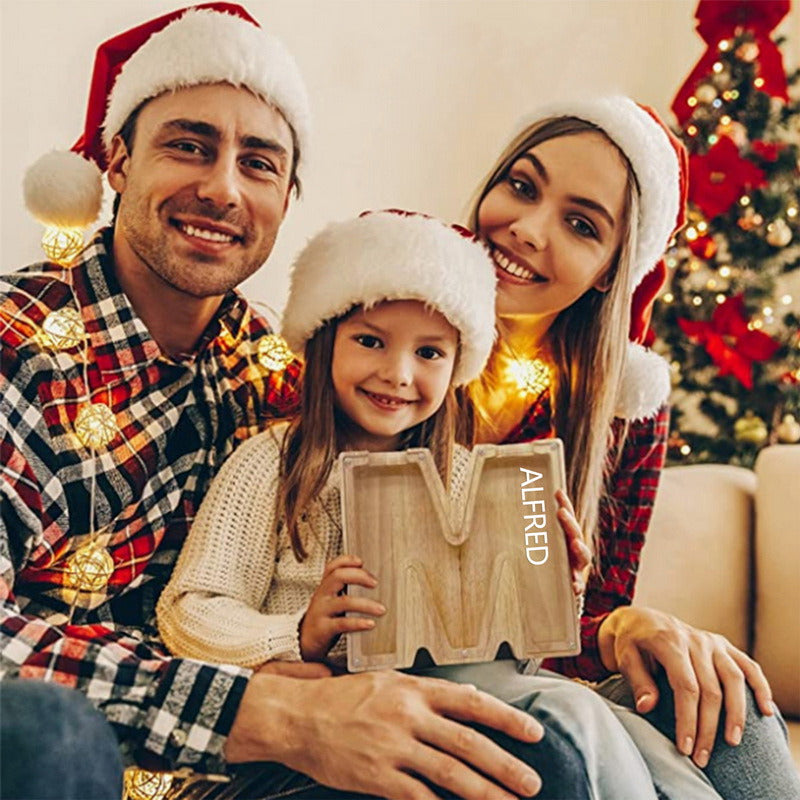 Une famille de trois souriants tenant une tirelire en bois pour l'alphabet d'une épargne.